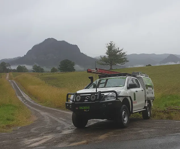 A Local Pest Experts ute on a rural road, with fields and a mountain behind it
