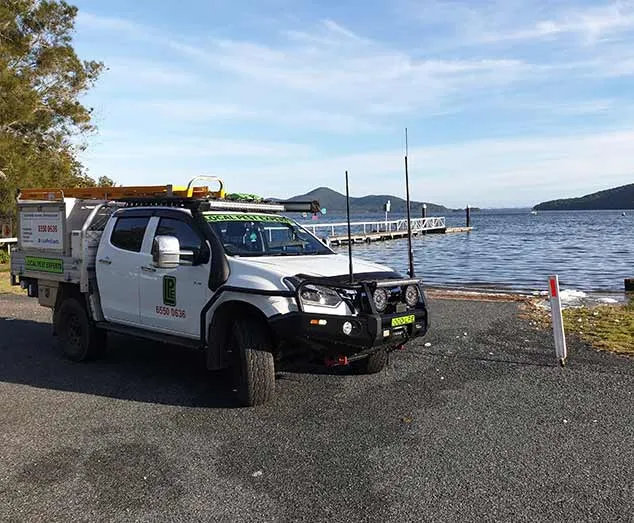 A Local Pest Experts ute parked beside the water and a jetty at Pacific Palms